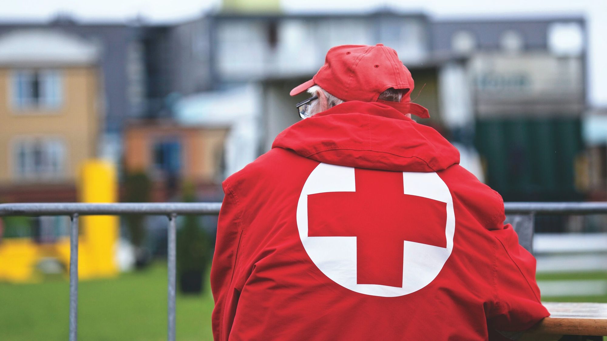 red cross member looking over buildings and a field during the day