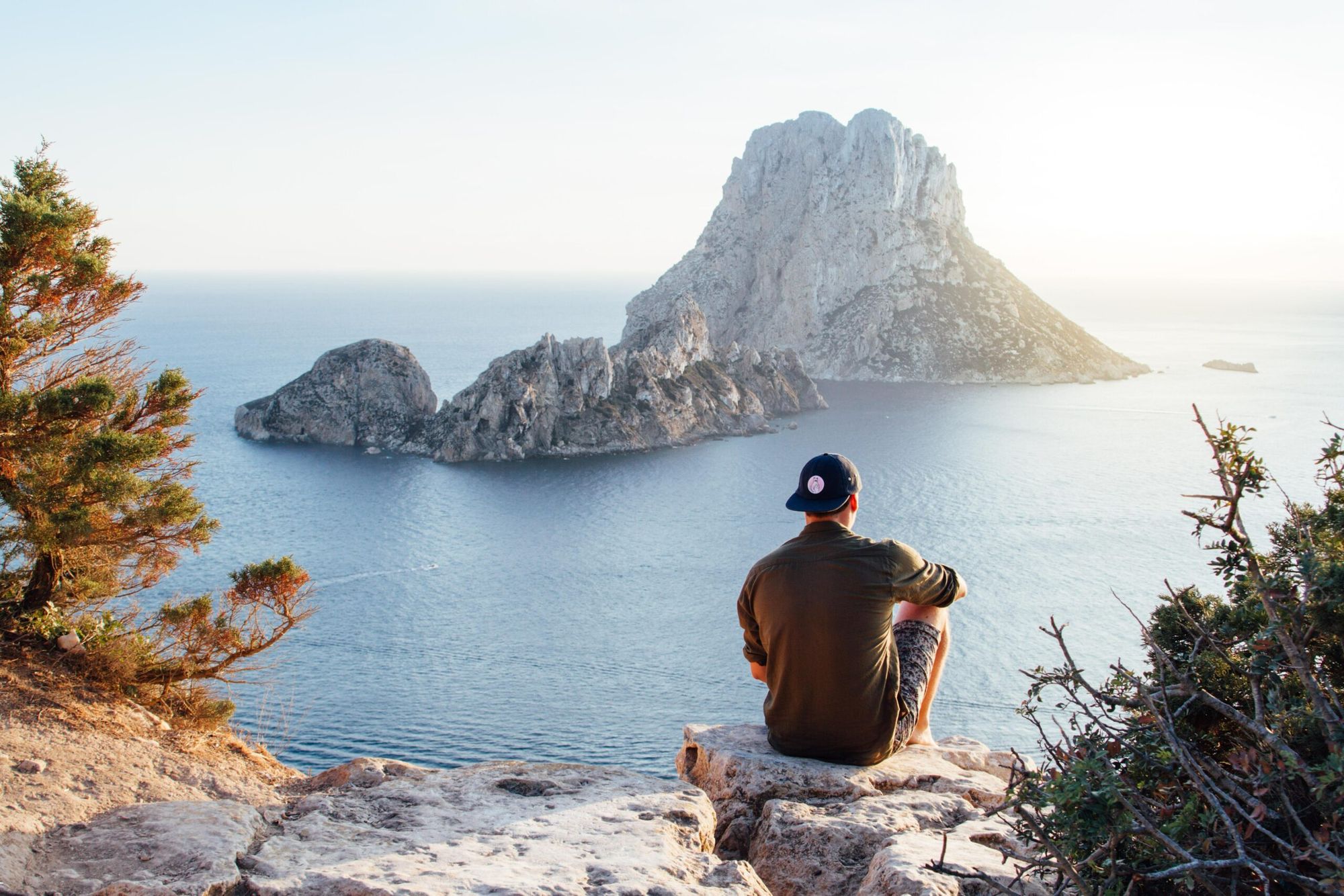 man sitting on ledge over looking a island among clear blue water. Stress relief 